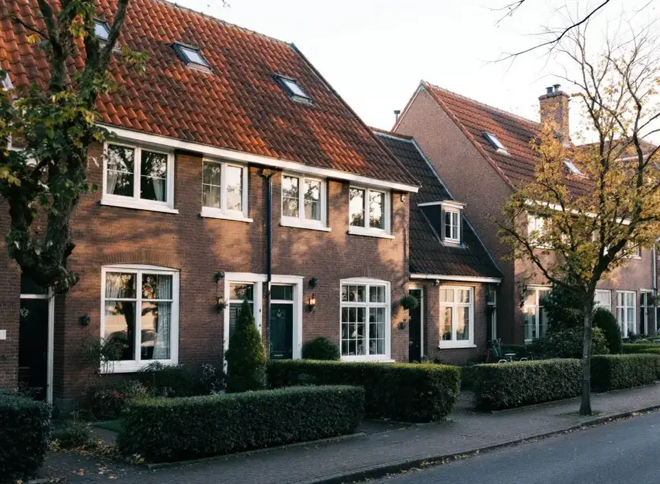 Rij jaren-dertigwoningen met steile oranje pannendaken, witte kozijnen met nieuw dubbel glas en lage hagen
